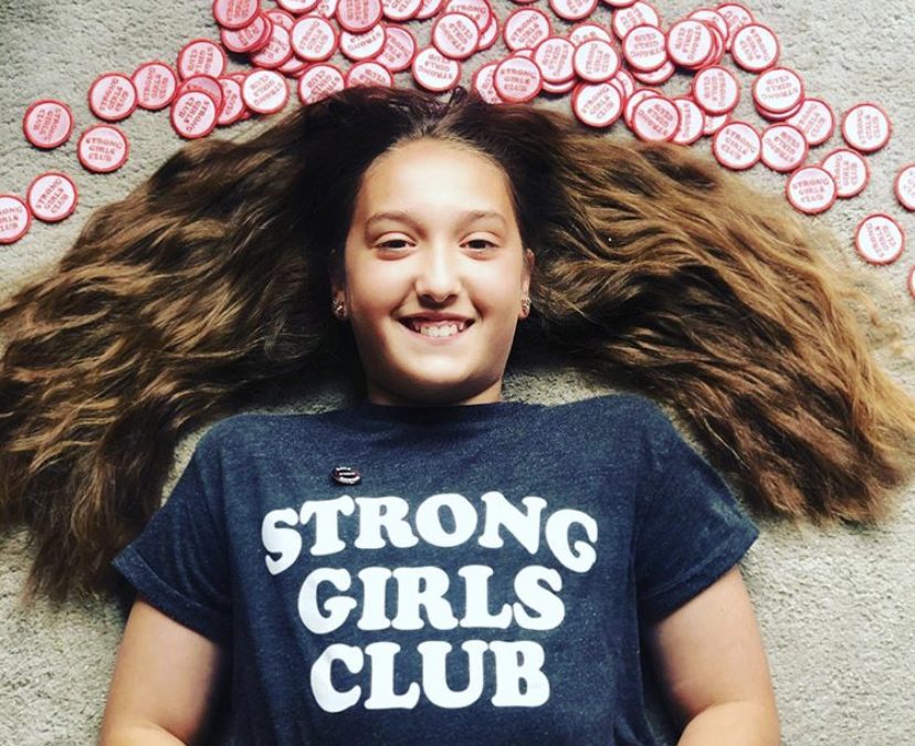 Smiling girl laying on floor surrounded by Strong Girls Club pin badges